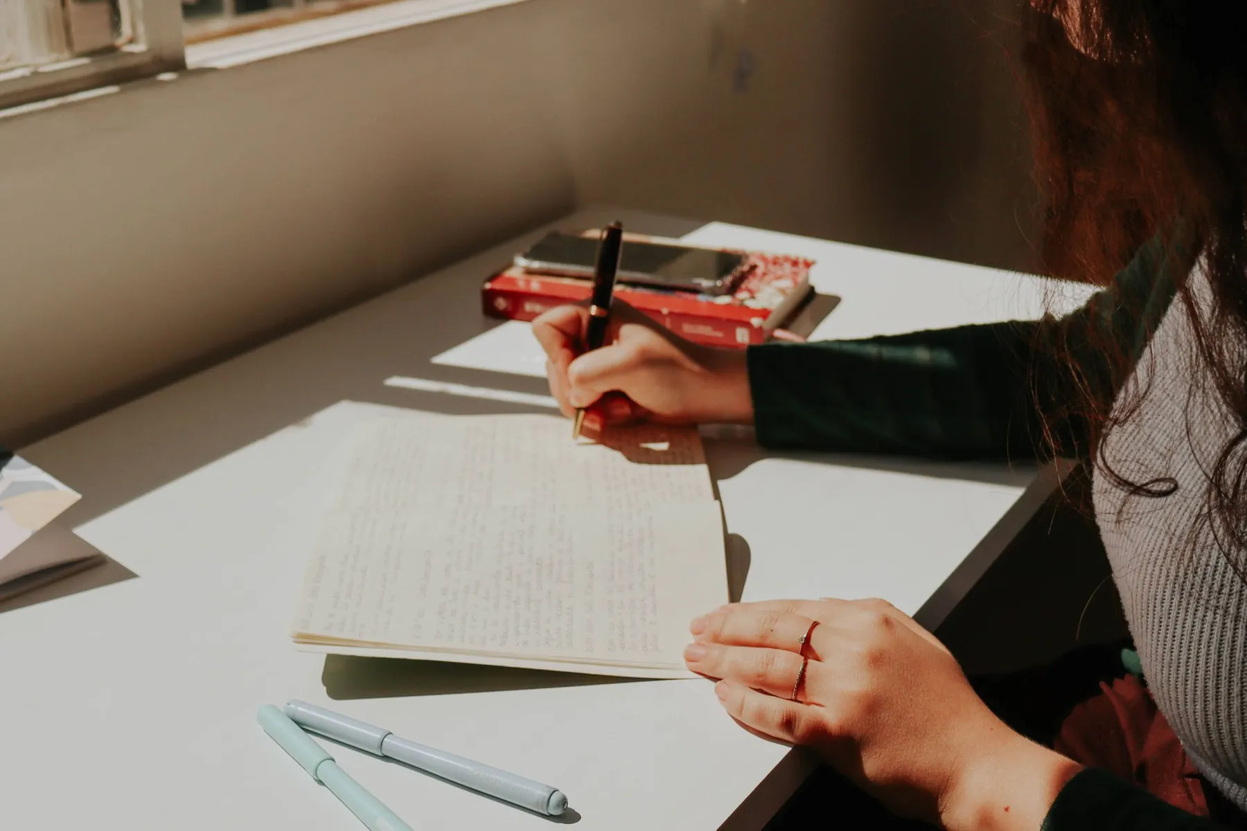 A person writing in a journal at a sunlit desk
