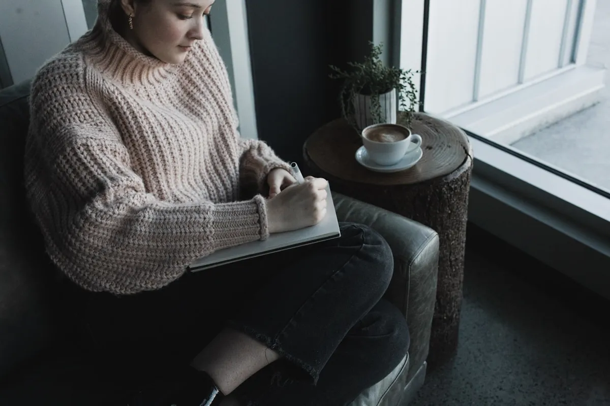 A person journaling with a cup of coffee by a window